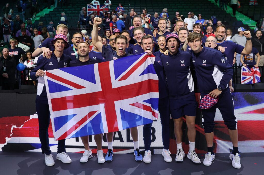 A jubilant British team celebrating with a Union Jack flag at a sporting event.