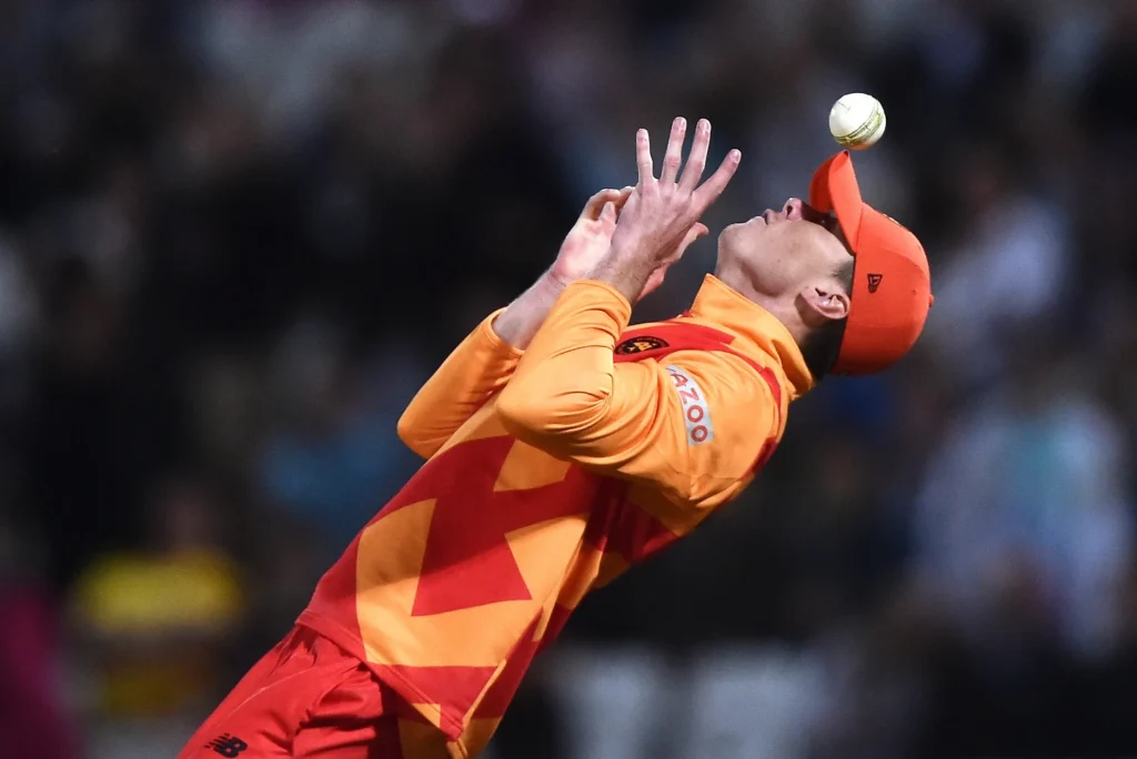 A cricket player attempting to catch a ball during a match.
