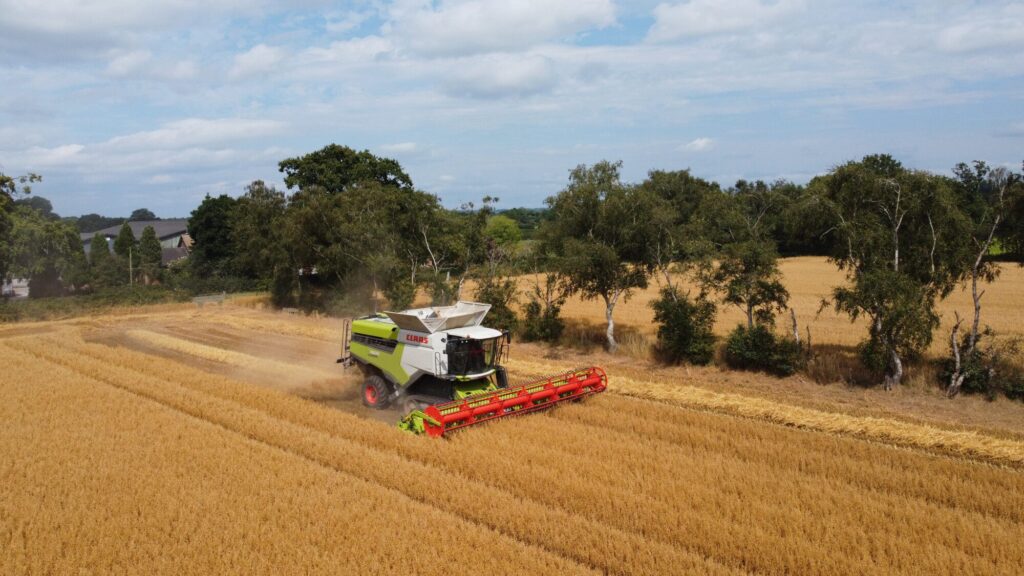 Aerial view of an agricultural machine harvesting wheat in a rural landscape.