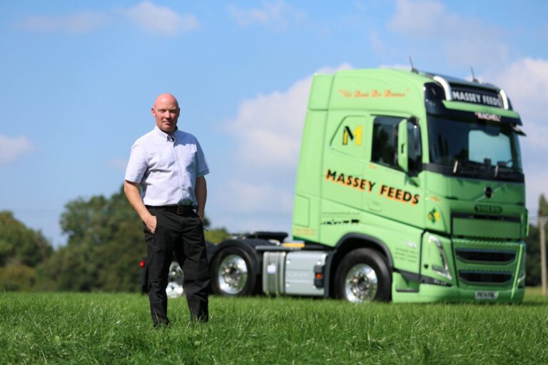 A man standing in a field with a green Massey Feeds truck in the background.
