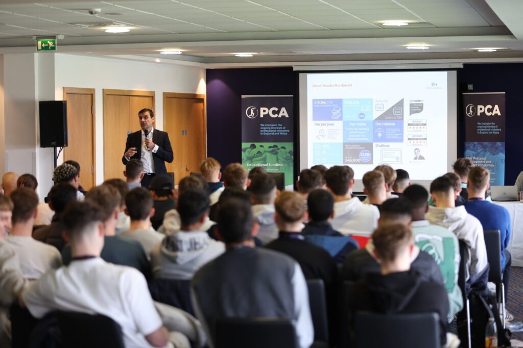 A speaker presenting at a PCA conference with an audience in attendance.