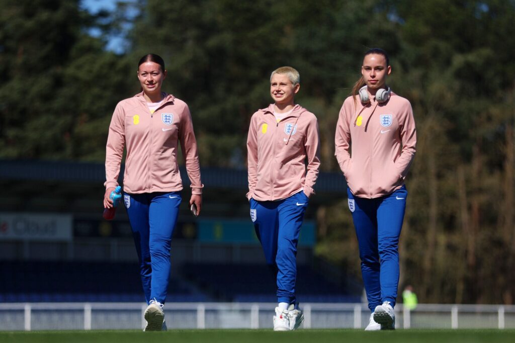 Three players from the England women's football team in training gear during a sunny day.