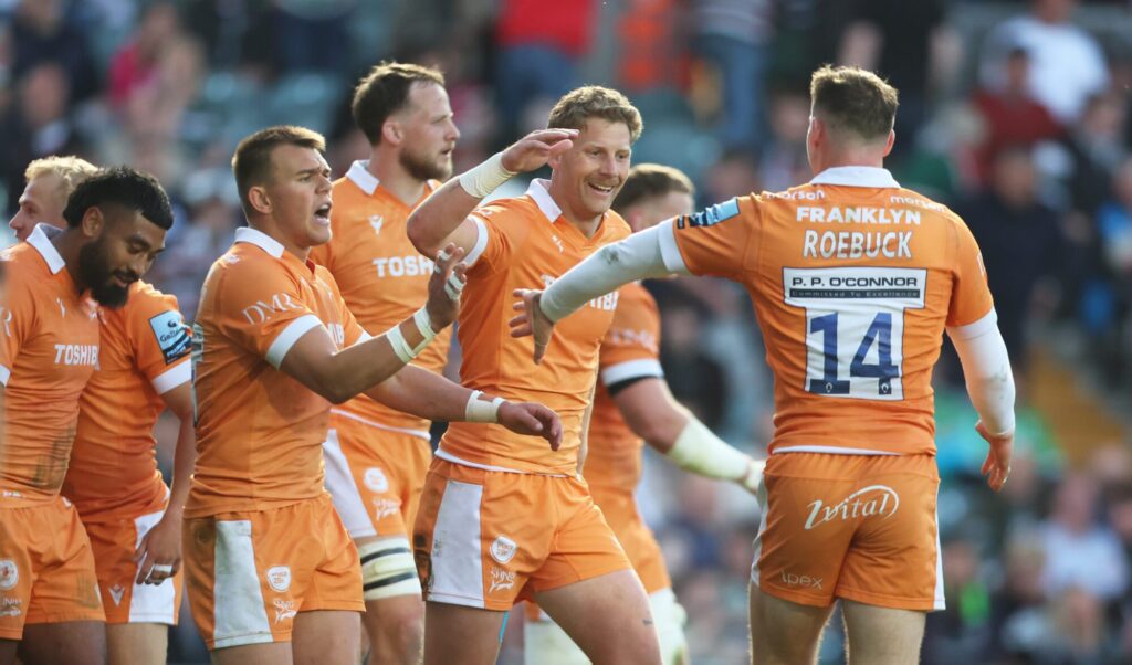 Rugby players in orange jerseys celebrating a successful play during a match.