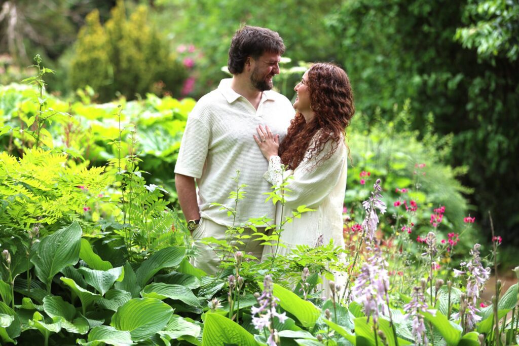 A romantic moment between Alice and Seb in a lush garden surrounded by greenery and flowers.