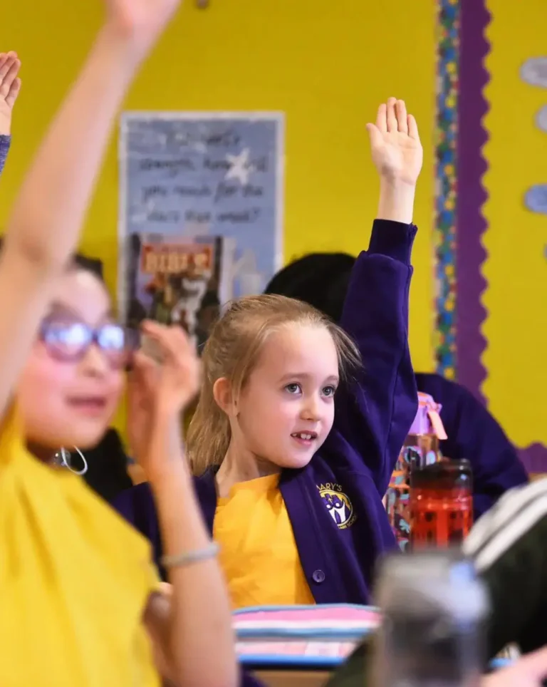 Children raising hands in a classroom setting.