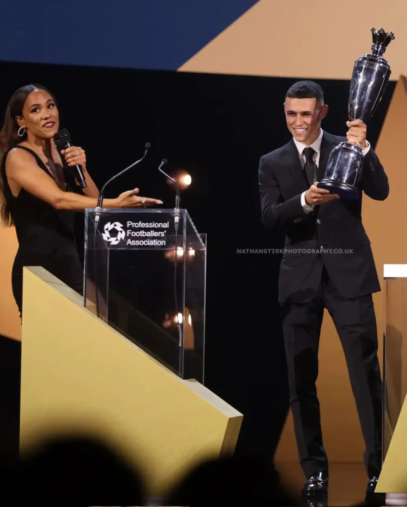 Celebrated footballer proudly holding a trophy during an awards ceremony.