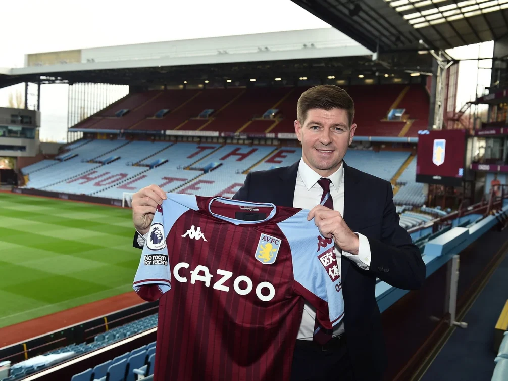 Steven Gerrard holding Aston Villa jersey at Villa Park.
