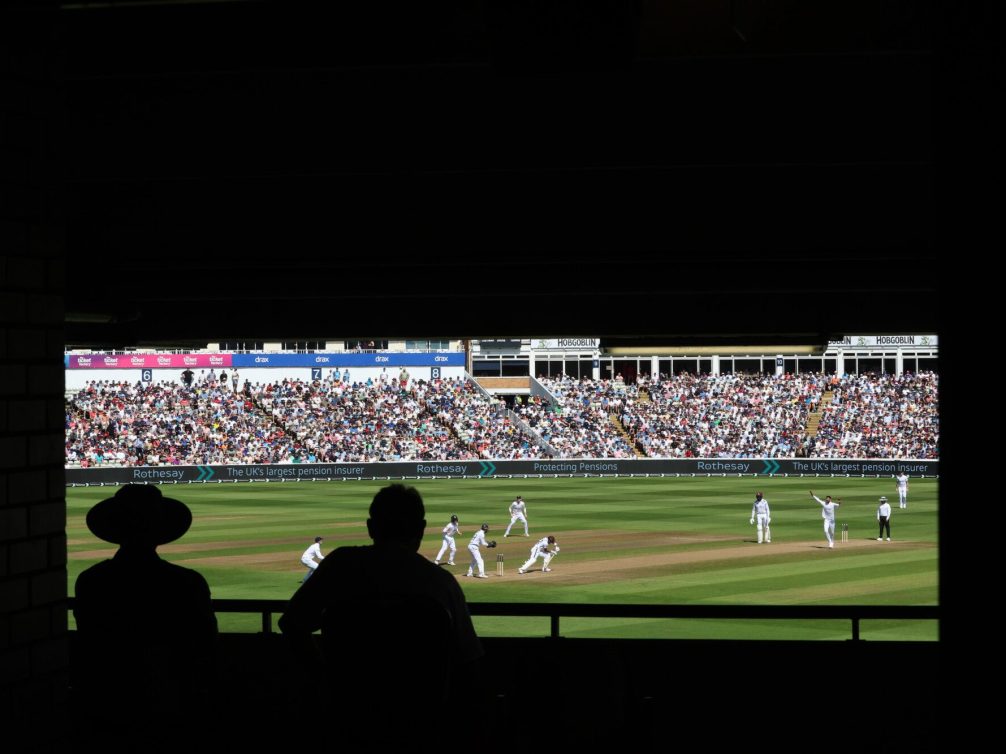 View of a cricket match with spectators in the stands.