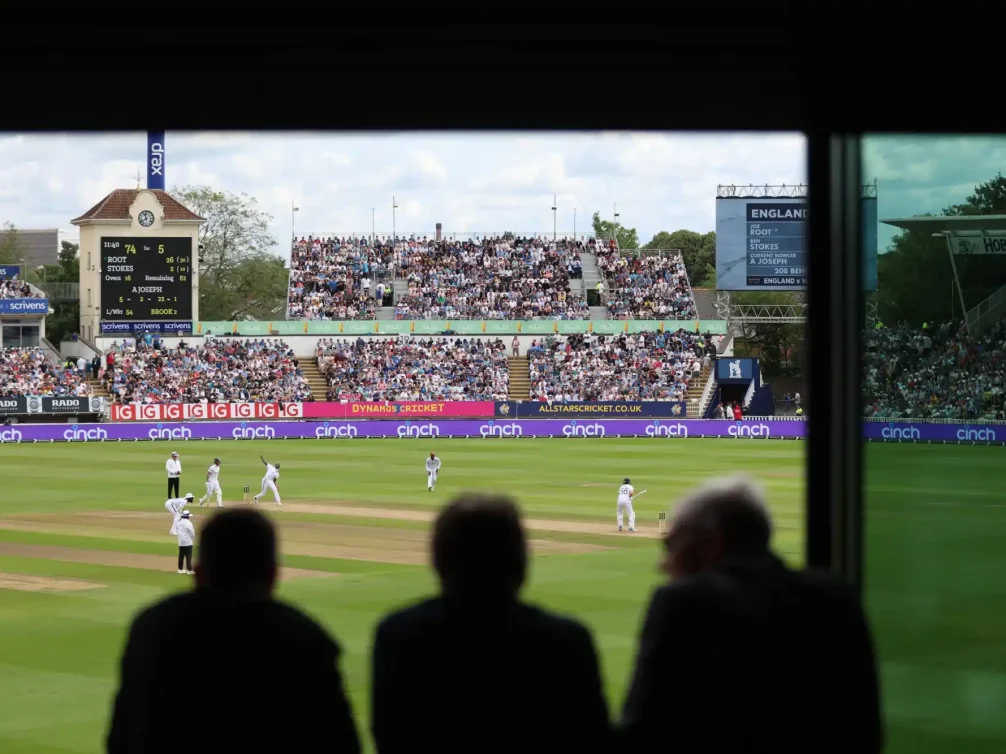 View of a cricket match from the stands with players on the field and a large crowd in attendance.