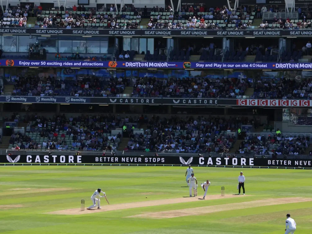 Cricketers in action on the field during a sunny day match.