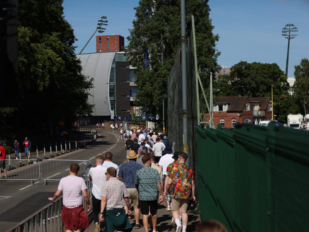 A crowd of people walking towards a stadium on a sunny day.