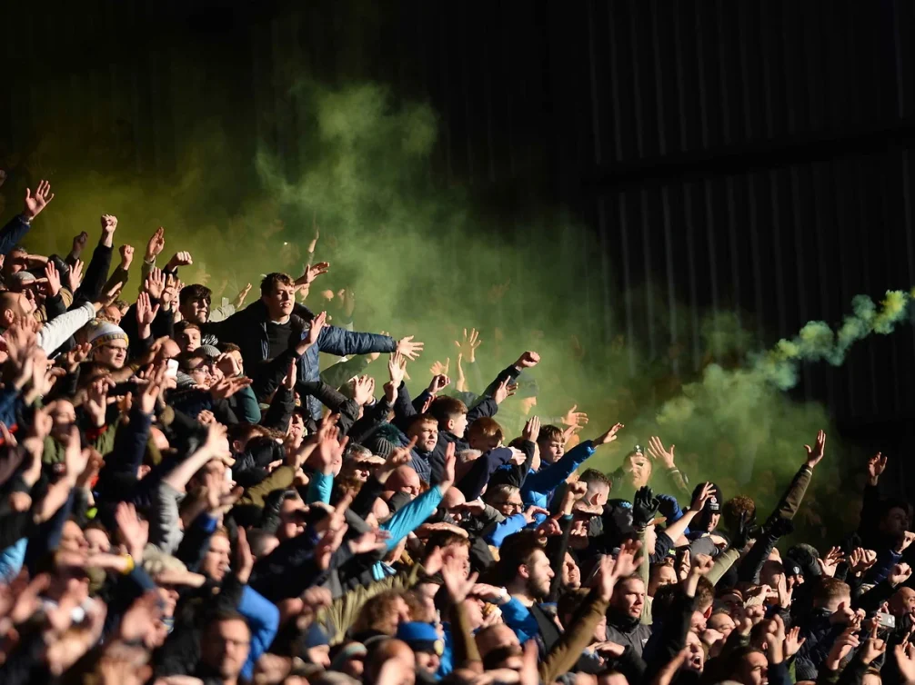 A vibrant crowd of football fans cheering with hands raised in excitement.