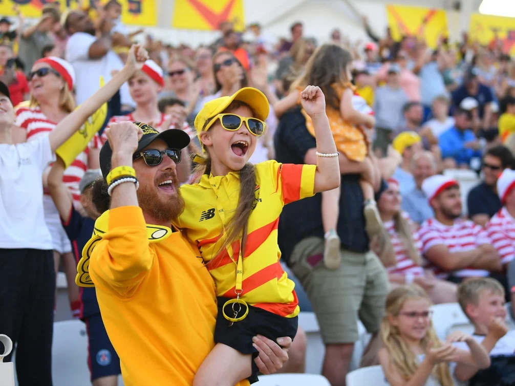 A father and daughter celebrating at a lively sports event, surrounded by enthusiastic fans.