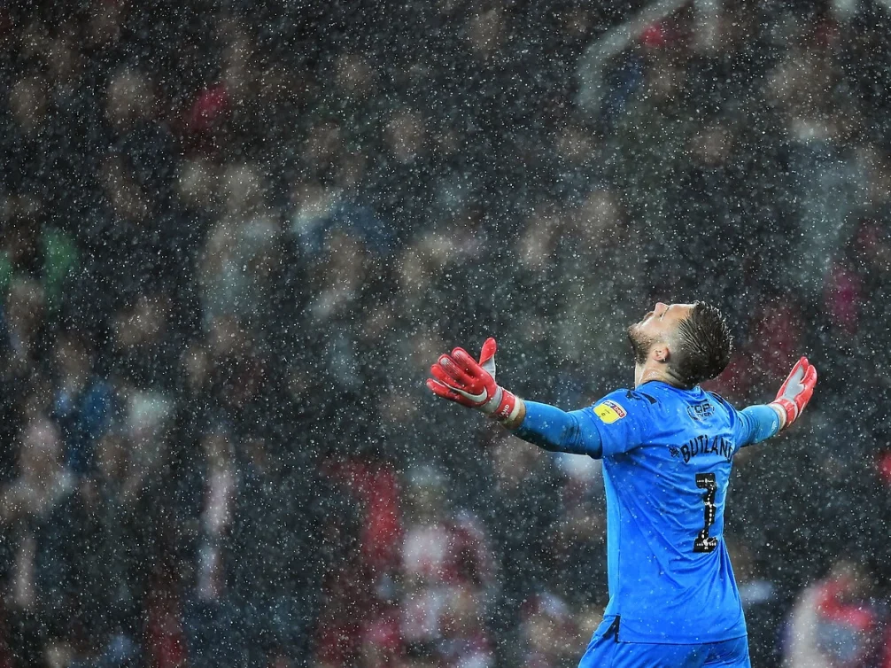A goalkeeper celebrating in the rain during a football match.