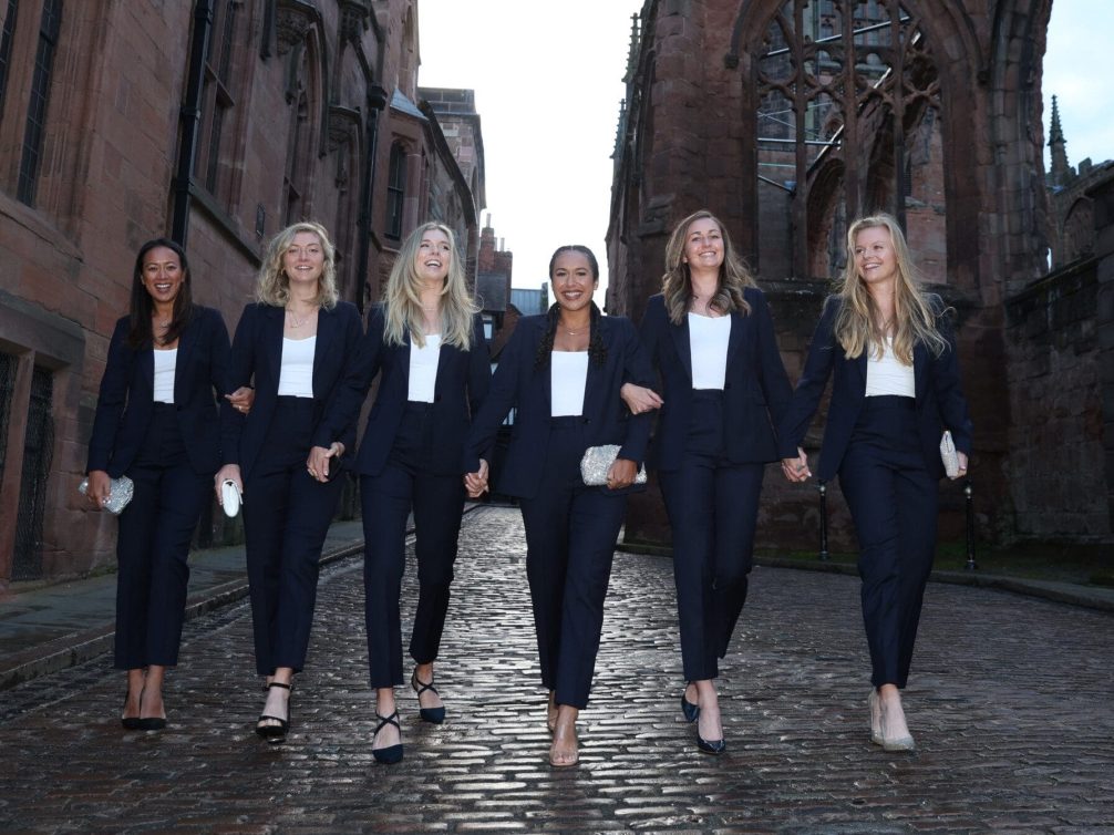 A group of stylish women walking together in matching suits on a cobblestone street.