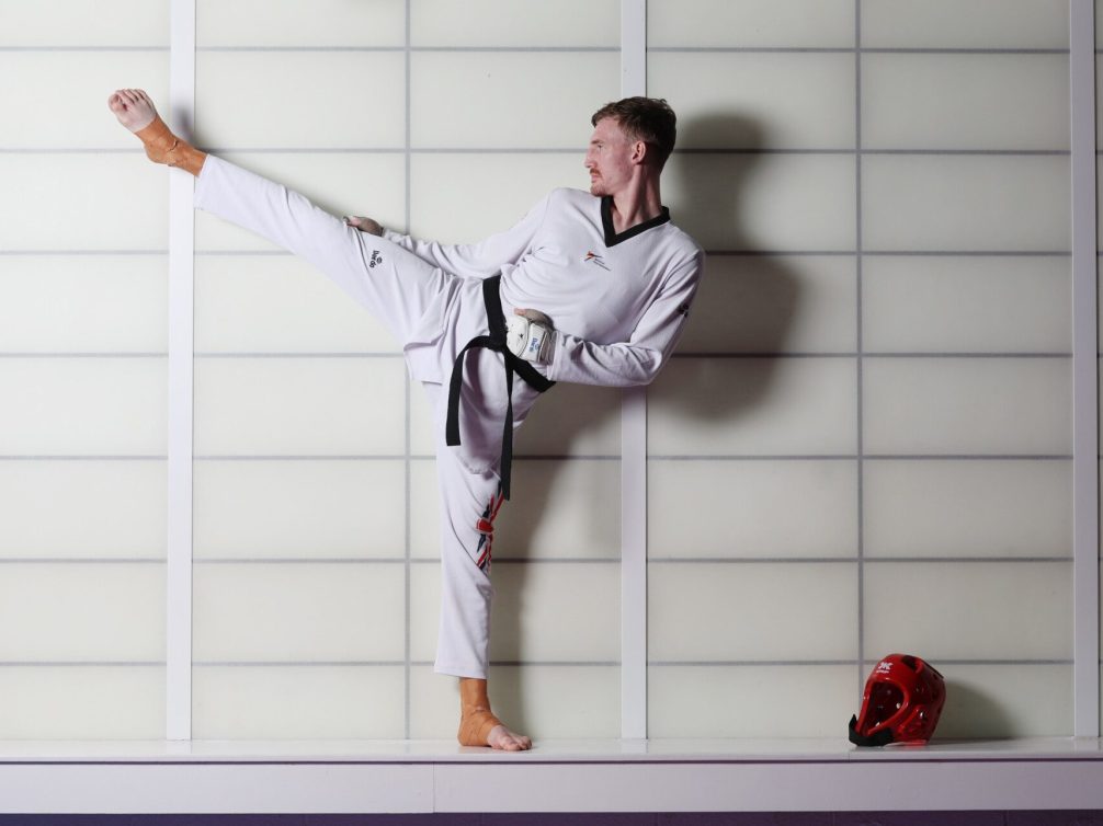 A taekwondo practitioner demonstrating a high kick in a studio setting.