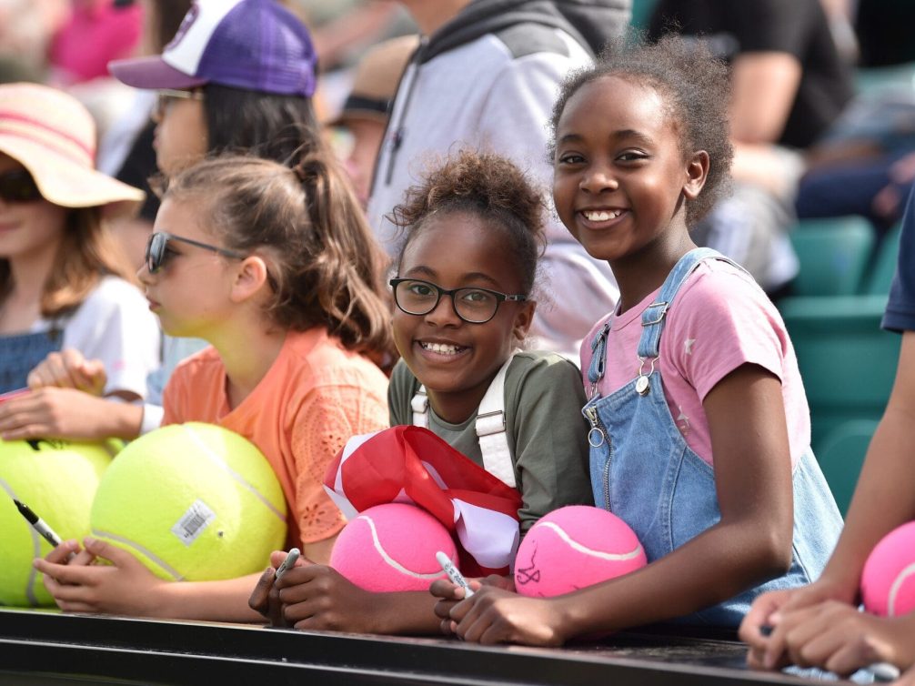 Young fans enjoying a tennis match with bright tennis balls.
